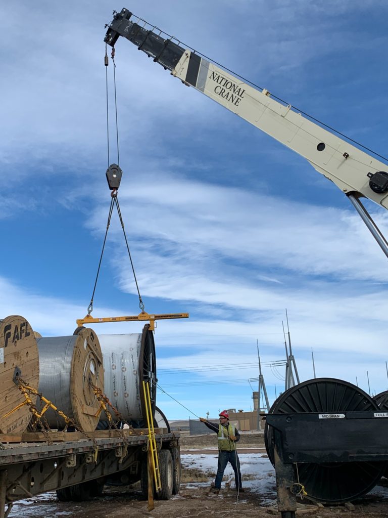 The crane hook lowers the wire rope slings and beam down to the reel.